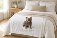 Load image into Gallery viewer, Charlie Bear plush blanket folded across the foot of a styled bed in a sunlit bedroom